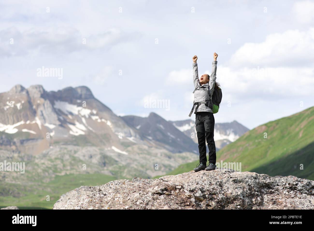 Excited hiker celebrating vacation raising arms in nature standing on the top of a rock Stock Photo
