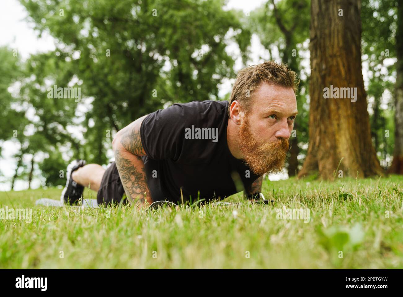 Ginger bearded man doing exercise during workout in park outdoors Stock Photo