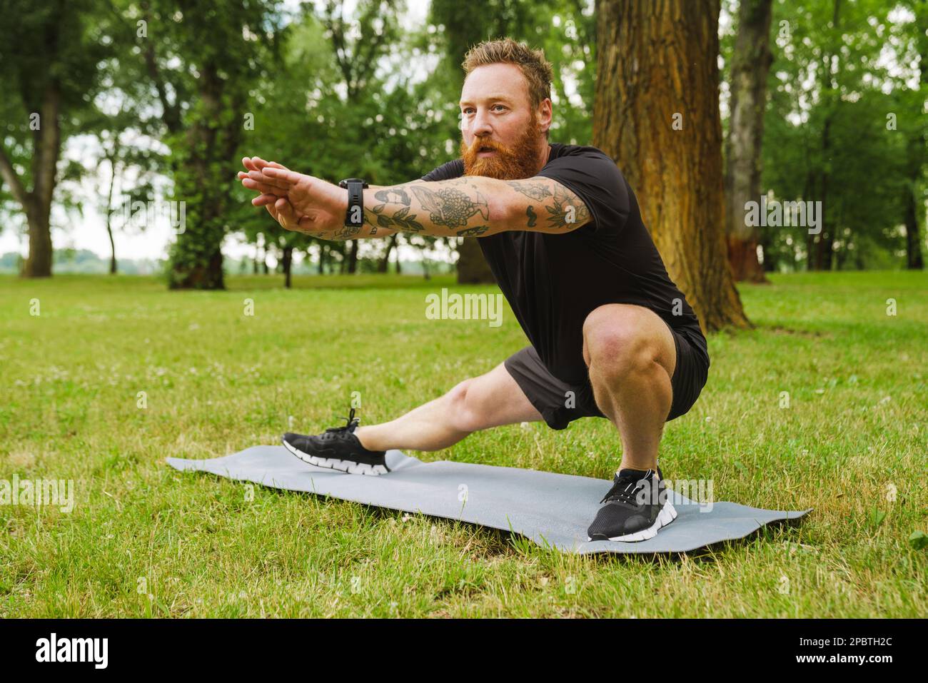 Ginger bearded man doing exercise during workout in park outdoors Stock Photo
