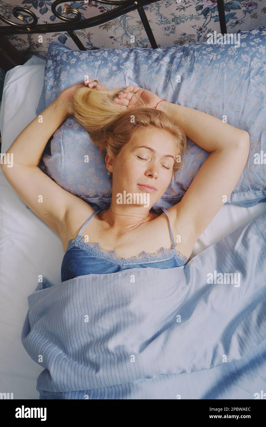 Mature middle aged woman stretching in bed waking up alone Stock Photo