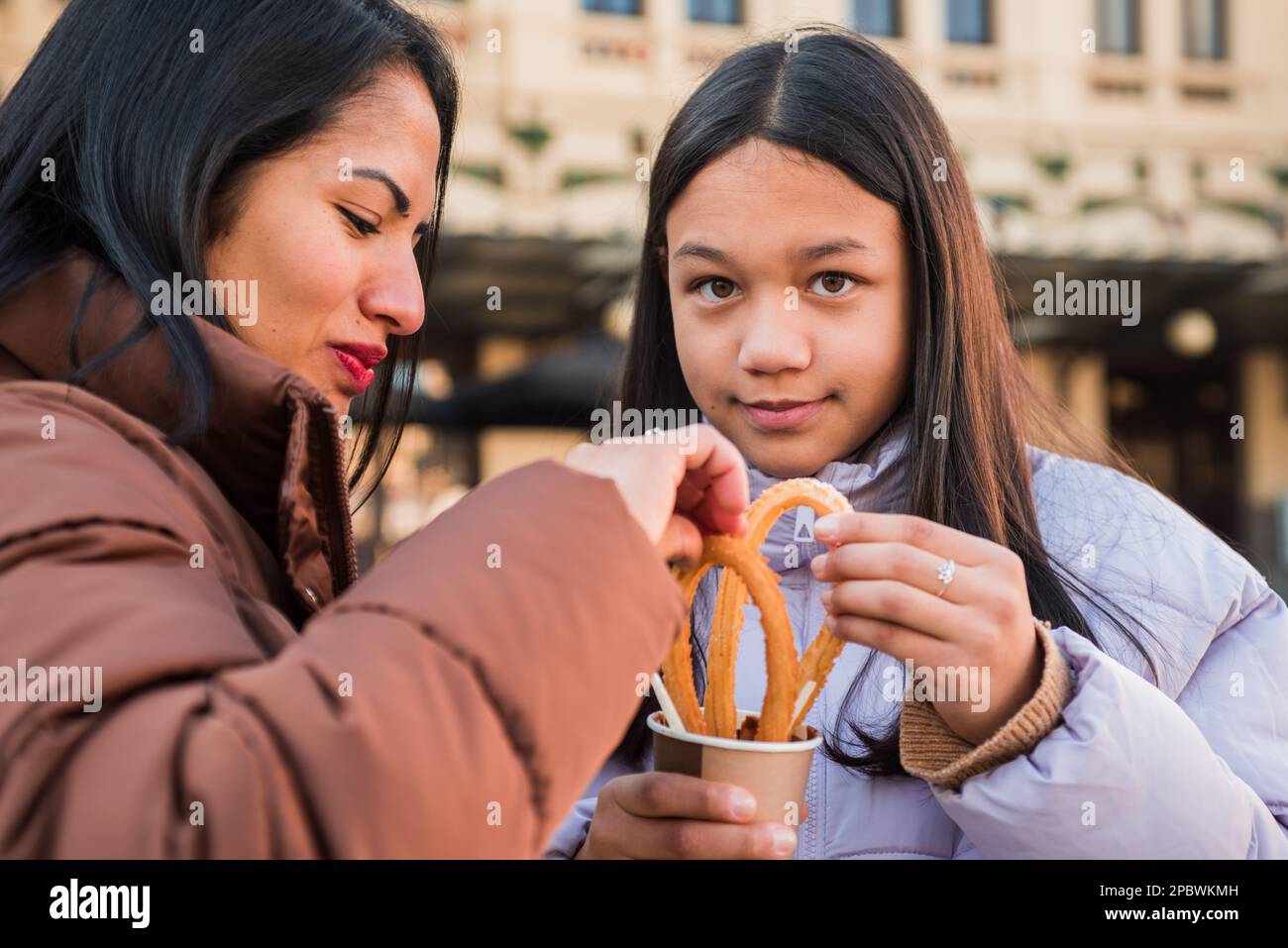 Teenager eating snack looking at camera with her mother. Stock Photo