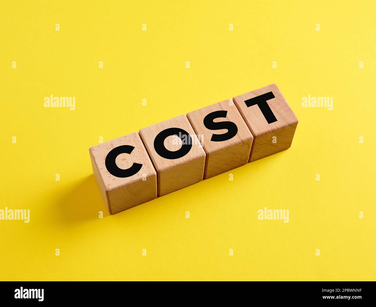 The word Cost on wooden cubes on yellow background. Business and financial costs concept. Stock Photo