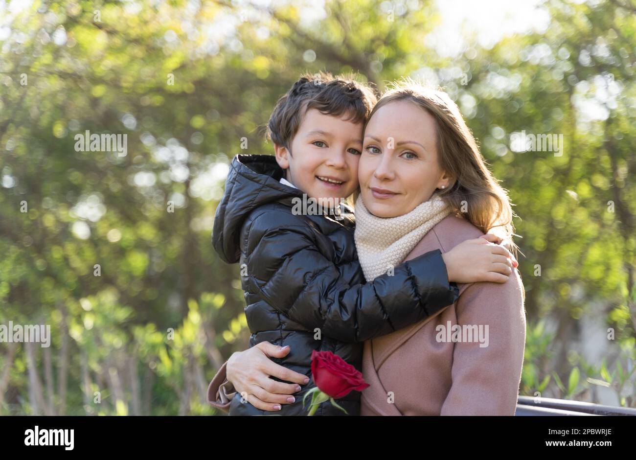 Boy and mother huging. Woman holding pink rose. Mother day Stock Photo