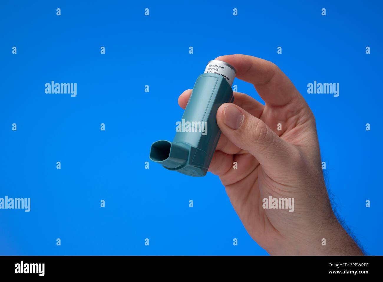 Asthma inhaler, generic, non-branded, held in hand by male hand. Close up studio shot, isolated on blue background. Stock Photo