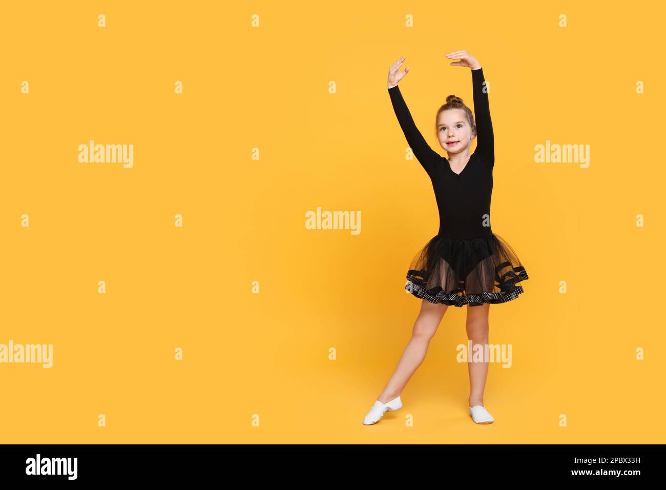 Cute little girl in black dress dancing on yellow background. Space for