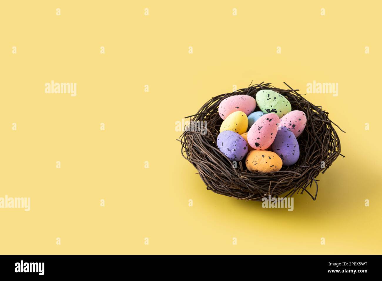Colorful Easter eggs inside a nest on yellow background. Copy space Stock Photo