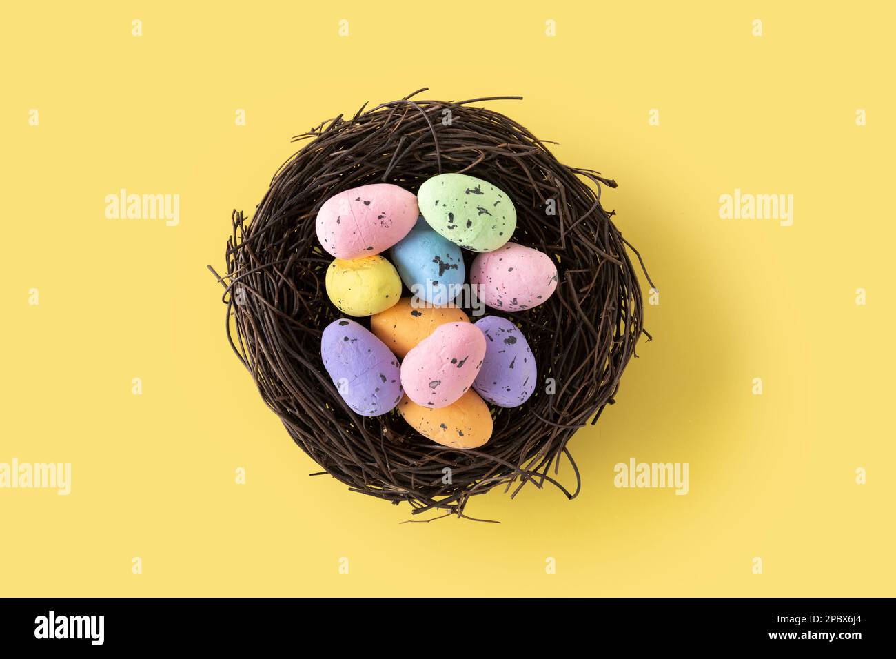Colorful Easter eggs inside a nest on yellow background. Copy space Stock Photo