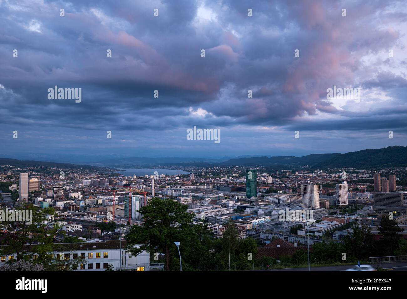 High overview of Zurich city Switzerland at dusk. Evening light, pink clouds, moody atmosphere, top view, vista point, no people. Stock Photo