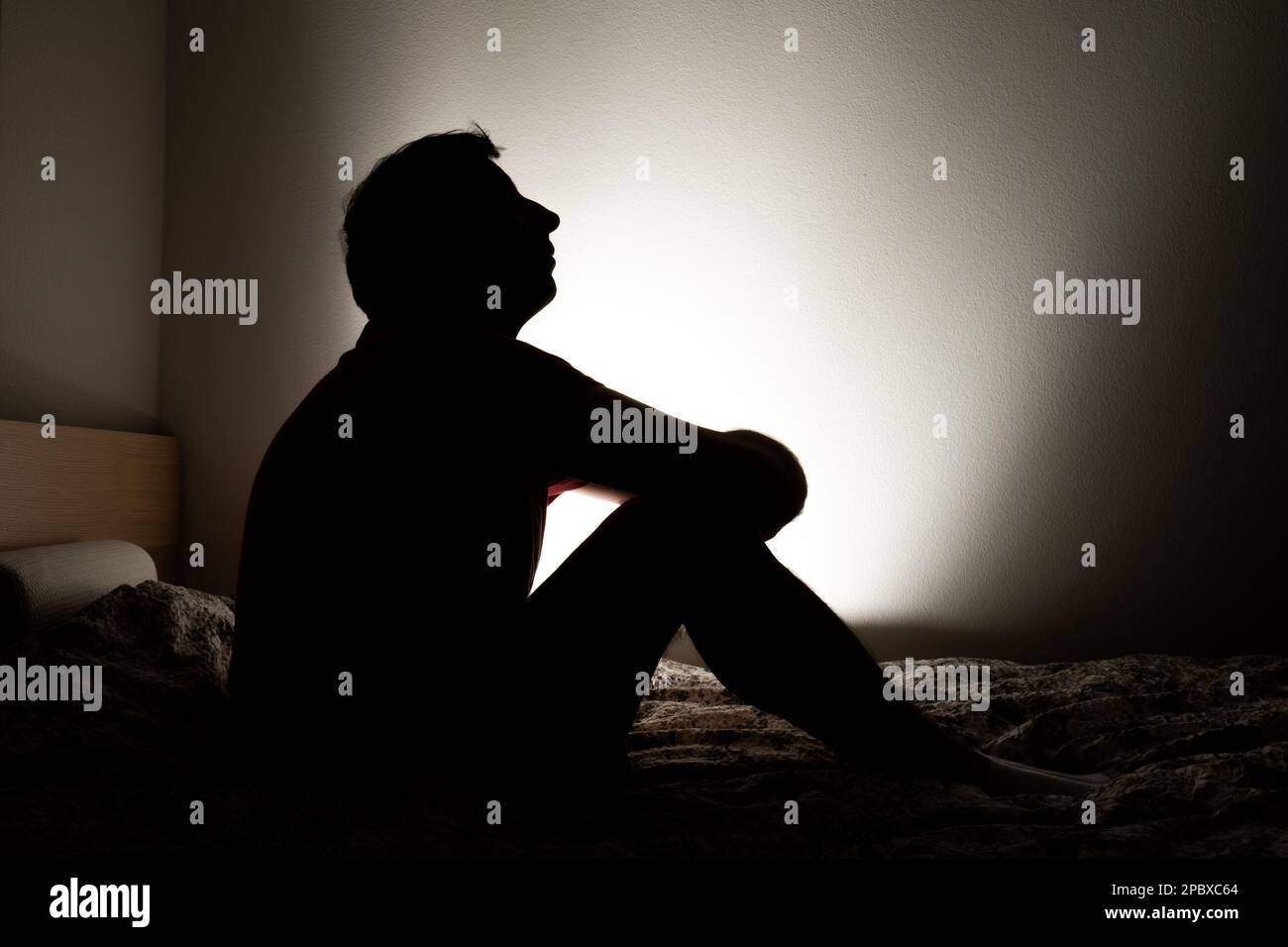 Male silhouette depicting loneliness or depression sitting in his apartment bed. Stock Photo