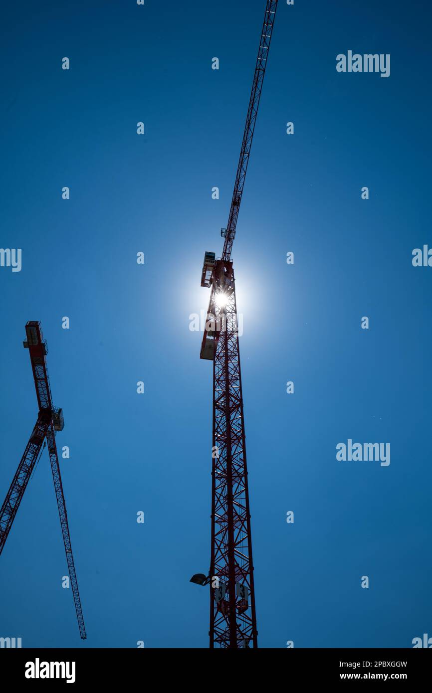 A pair of construction cranes set against the noon sun. Blue sky, no