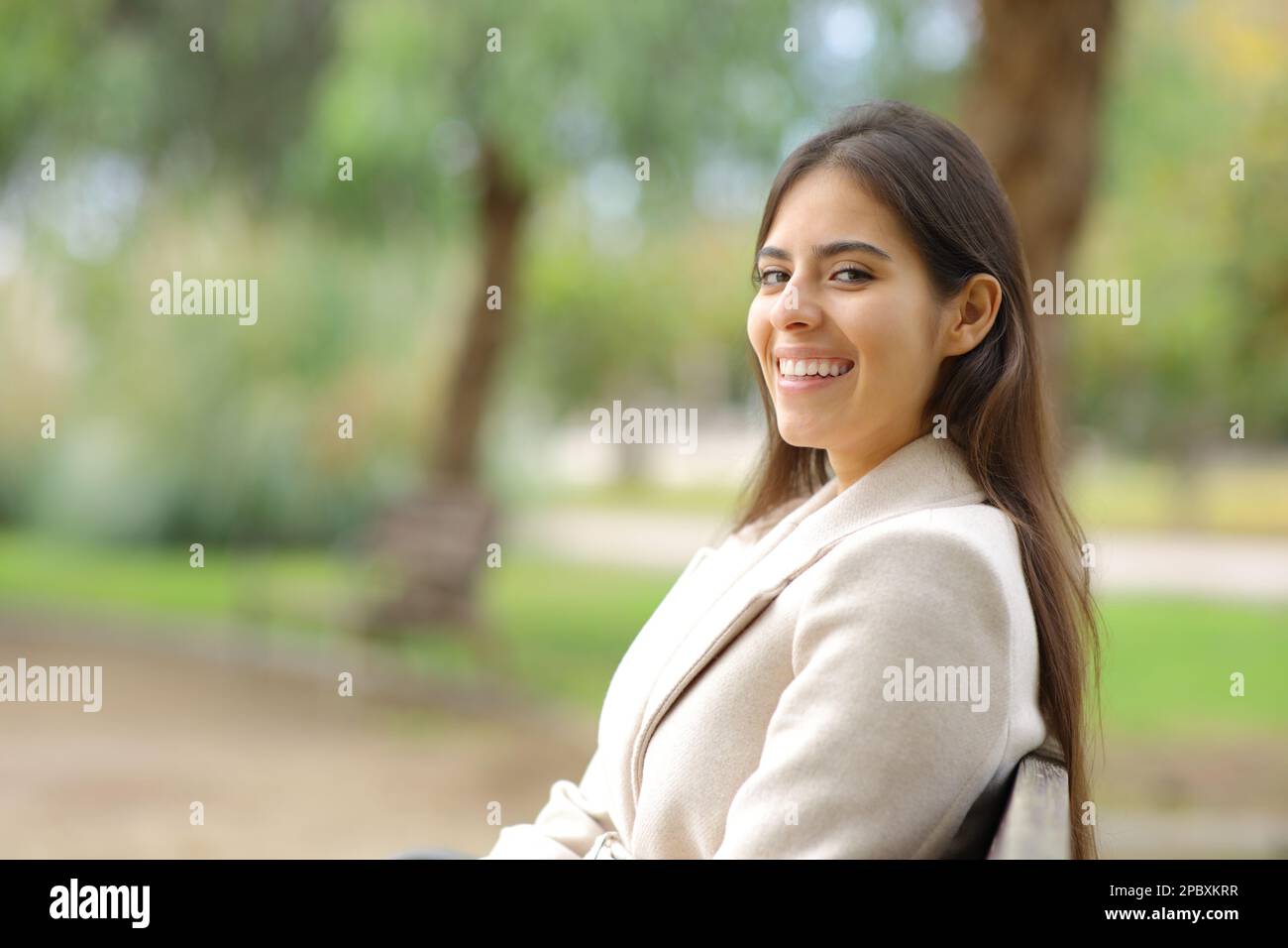 Happy woman in winter looking at camera sitting on a bench in a park Stock Photo