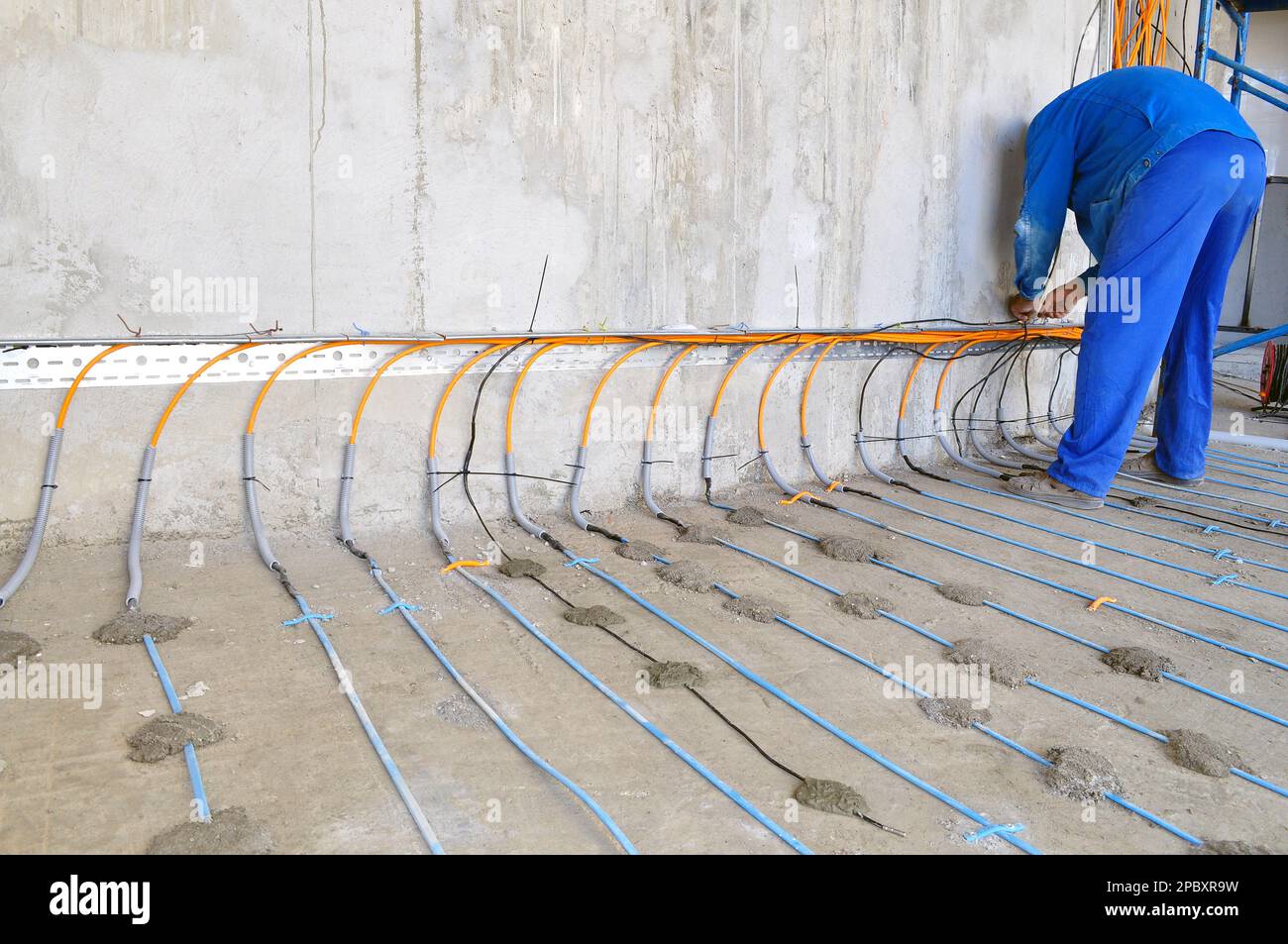 A worker in a blue uniform is engaged in laying a floor heating cable on concrete, a man from the back Stock Photo