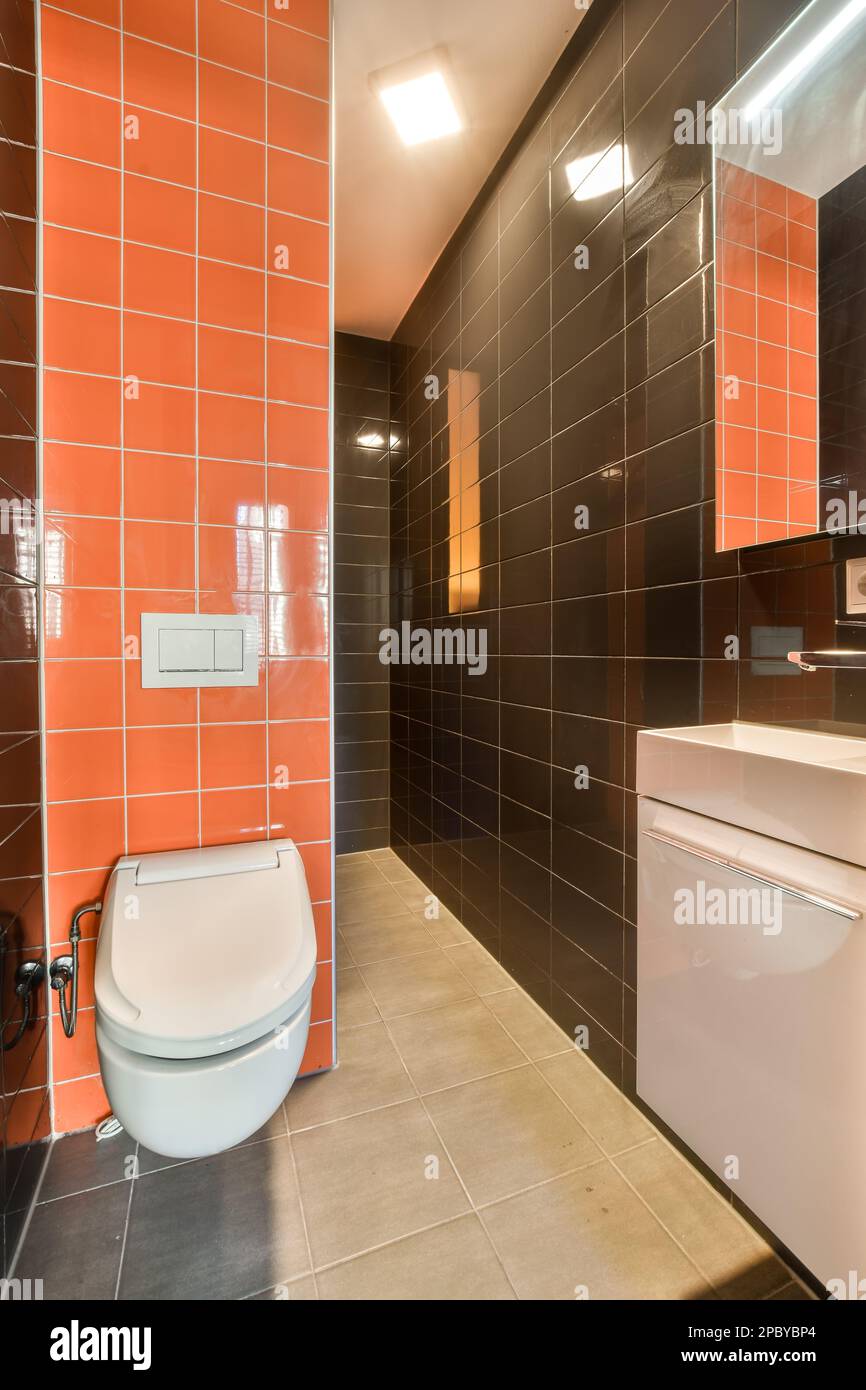 Modern restroom with orange and black tiled walls and white ceramic toilet  placed near sink under hanging mirror Stock Photo - Alamy, image size:866x1390