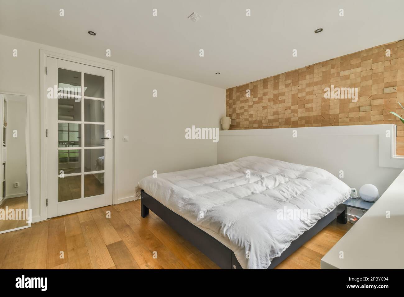 Comfortable bed with soft blanket placed near window and brick wall in light bedroom interior with minimalist style Stock Photo