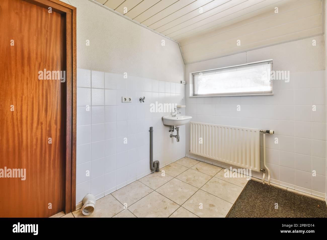 Interior design of light bathroom with sink and chrome faucet near radiator and wooden door decorated with ceramic tile and gray rug Stock Photo