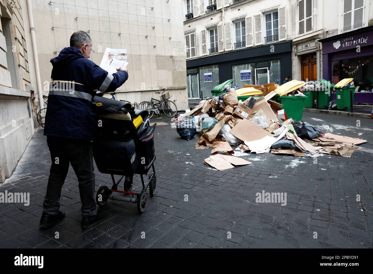 People walk in a street where garbage cans are overflowing, as garbage has not been collected, in Paris, France March 13, 2023. REUTERS/Benoit Tessier Stock Photo