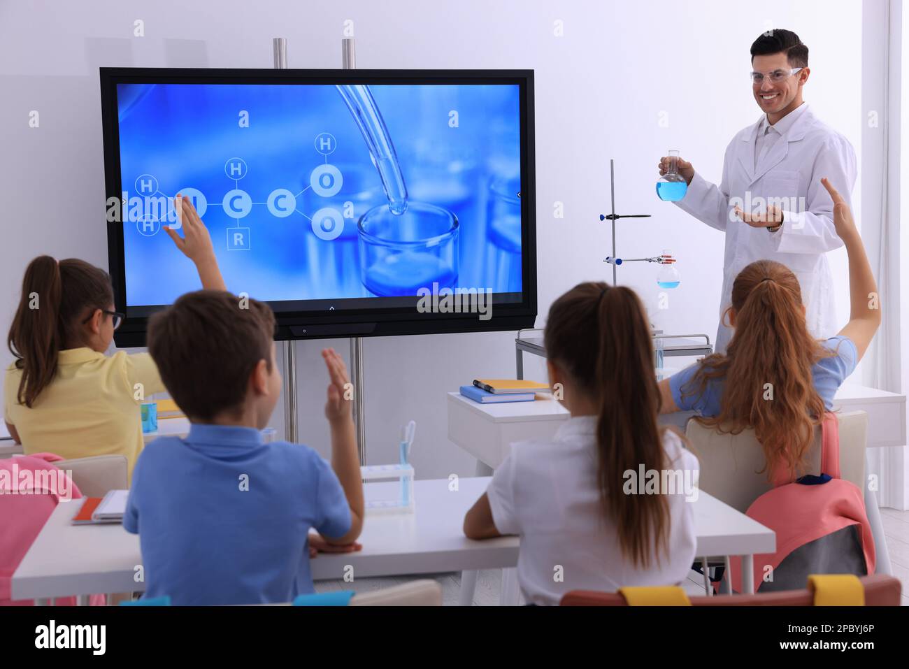 Teacher holding flask with solution near interactive board in classroom during practical lesson Stock Photo