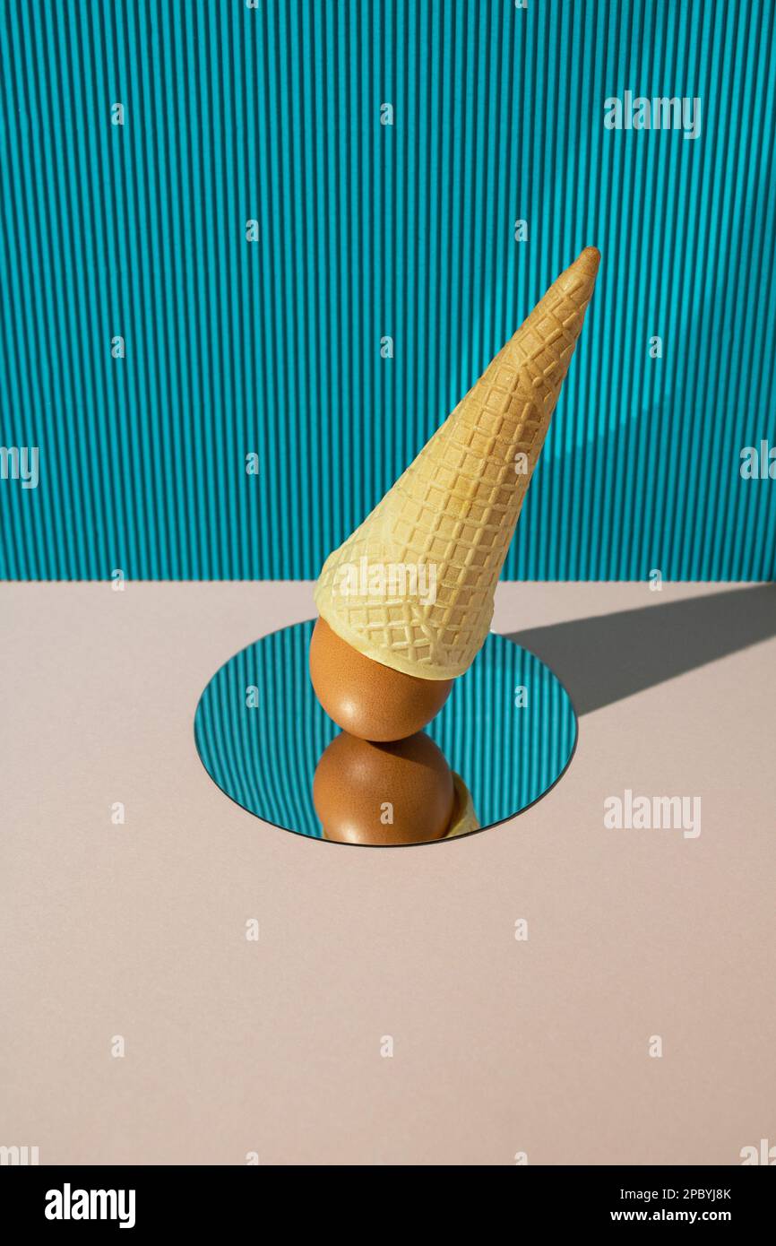 Fresh chicken egg with ice cream cone reflecting in mirror on blue and