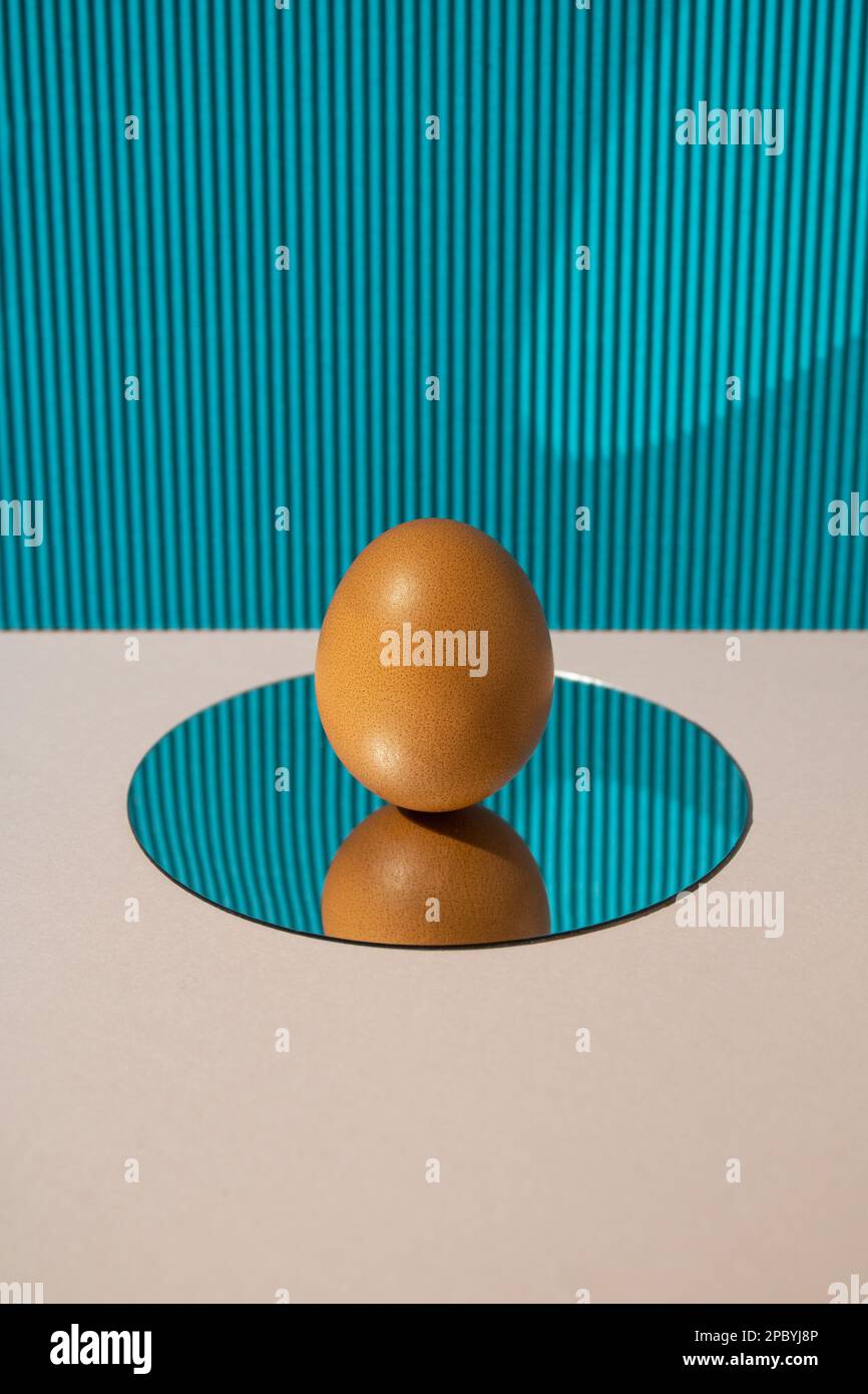 Fresh chicken egg reflecting in mirror on blue and beige background. Minimal concept. Stock Photo