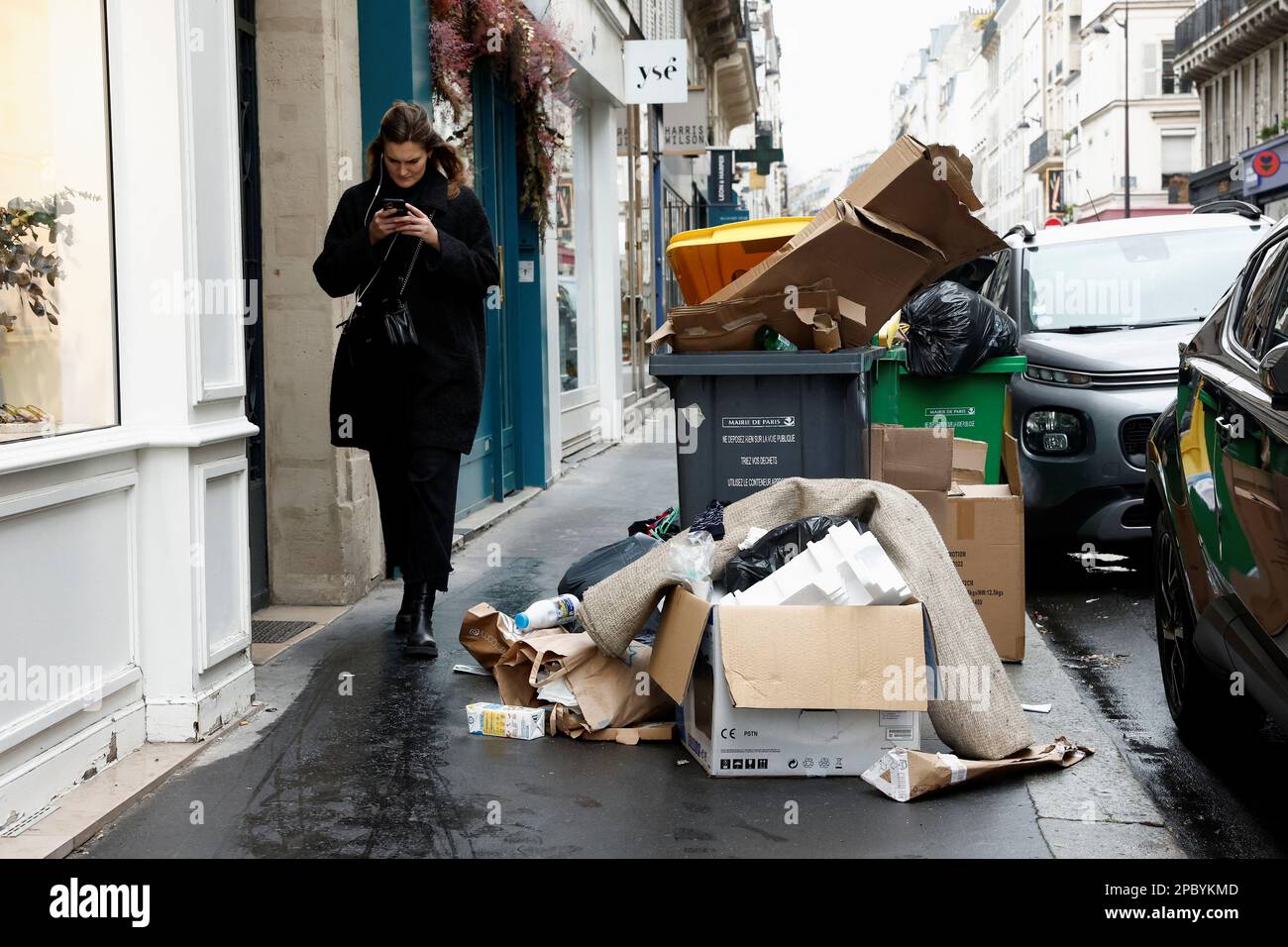 People walk in a street where garbage cans are overflowing, as garbage has not been collected, in Paris, France March 13, 2023. REUTERS/Benoit Tessier Stock Photo