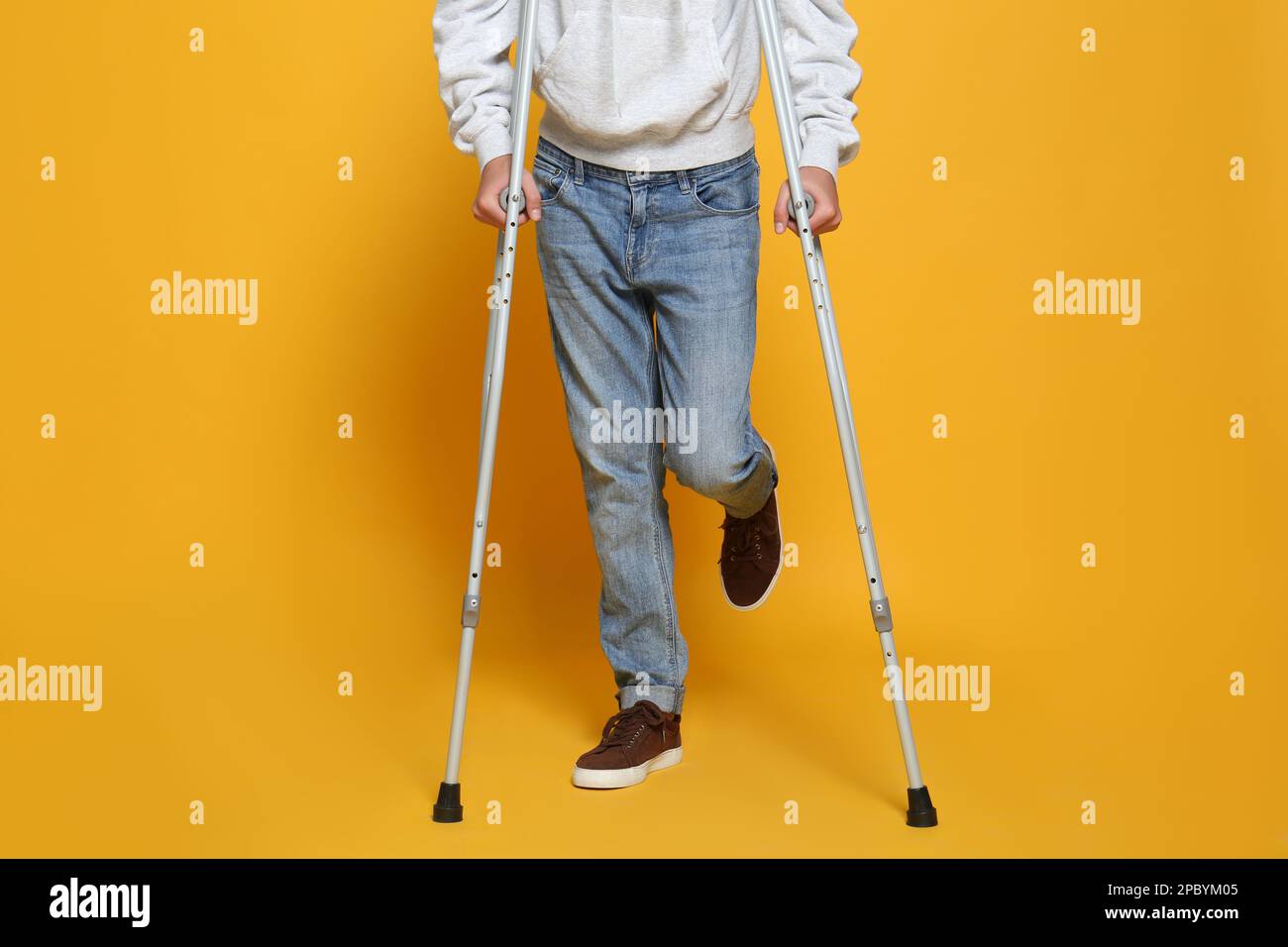 Man with injured leg using crutches on yellow background, closeup Stock