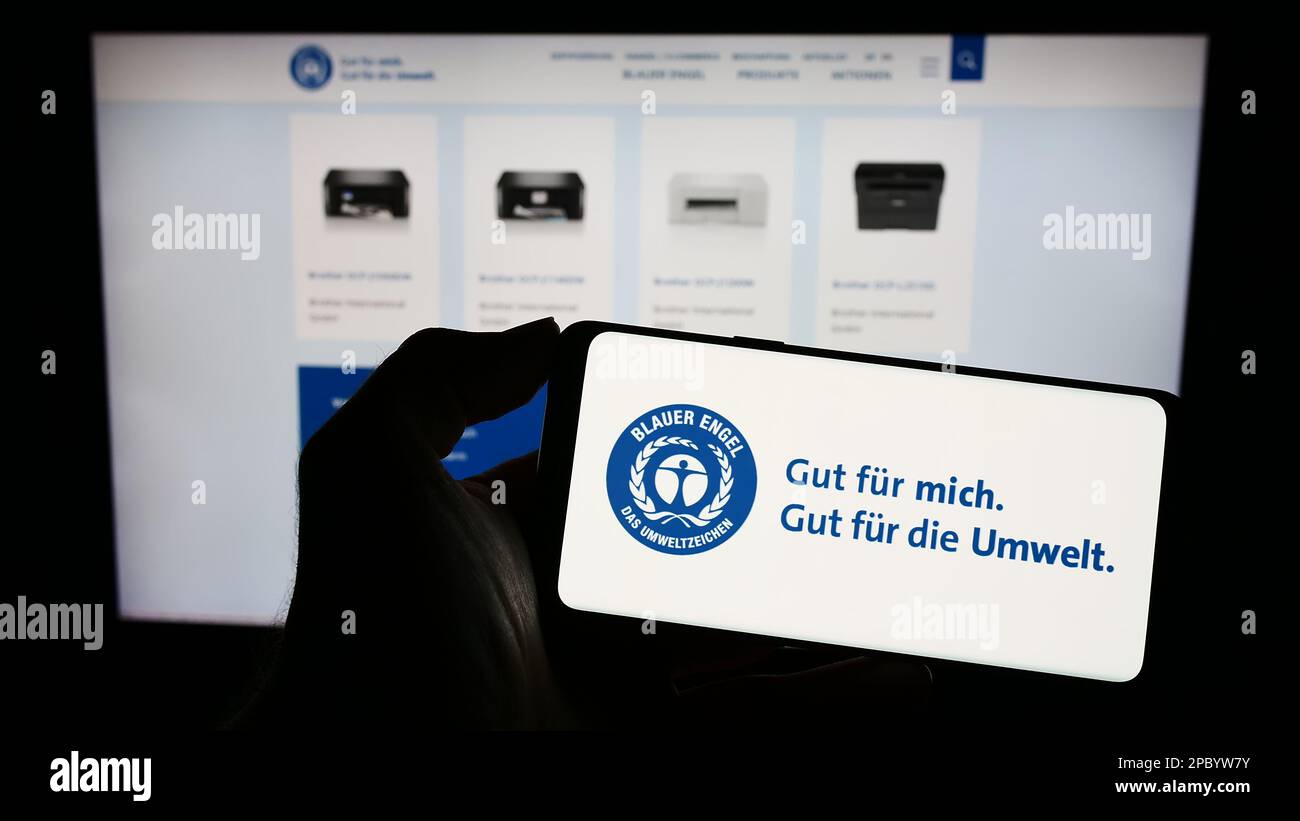 Person holding mobile phone with logo of German environmental label Blauer Engel (Blue Angel) on screen with web page. Focus on phone display. Stock Photo
