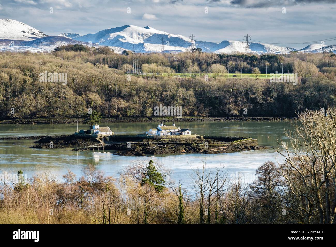 Scenic view to Ynys Gored Goch (Red Weirisland) in Menai Strait with snow on Snowdon in Snowdonia mountains in winter. Menai Bridge Anglesey Wales UK Stock Photo