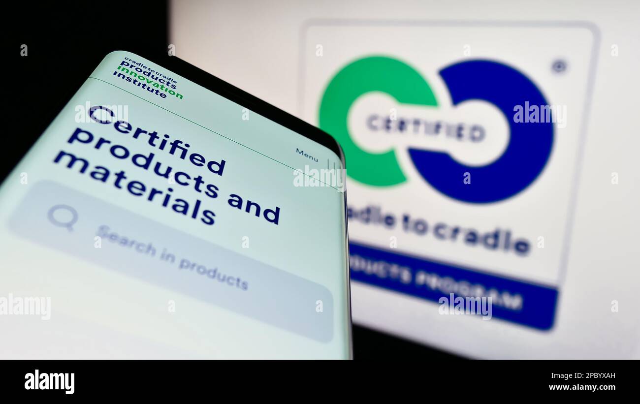 Smartphone with webpage of environmental label Cradle to Cradle Certified on screen in front of logo. Focus on top-left of phone display. Stock Photo