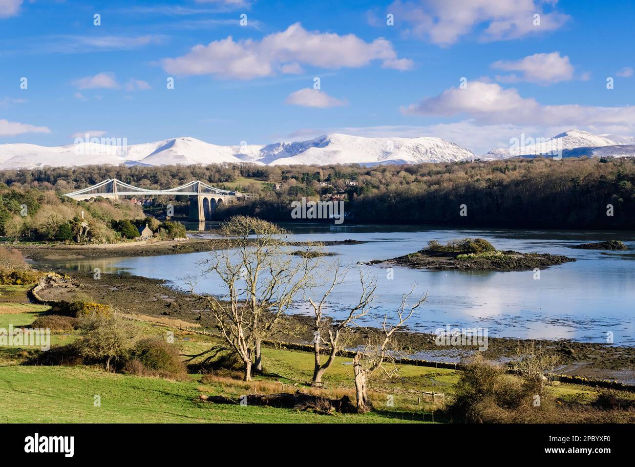 Scenic view to Menai Suspension bridge crossing Menai Strait with snow on mountains in winter. Menai Bridge (Porthaethwy), Isle of Anglesey, Wales, UK Stock Photo