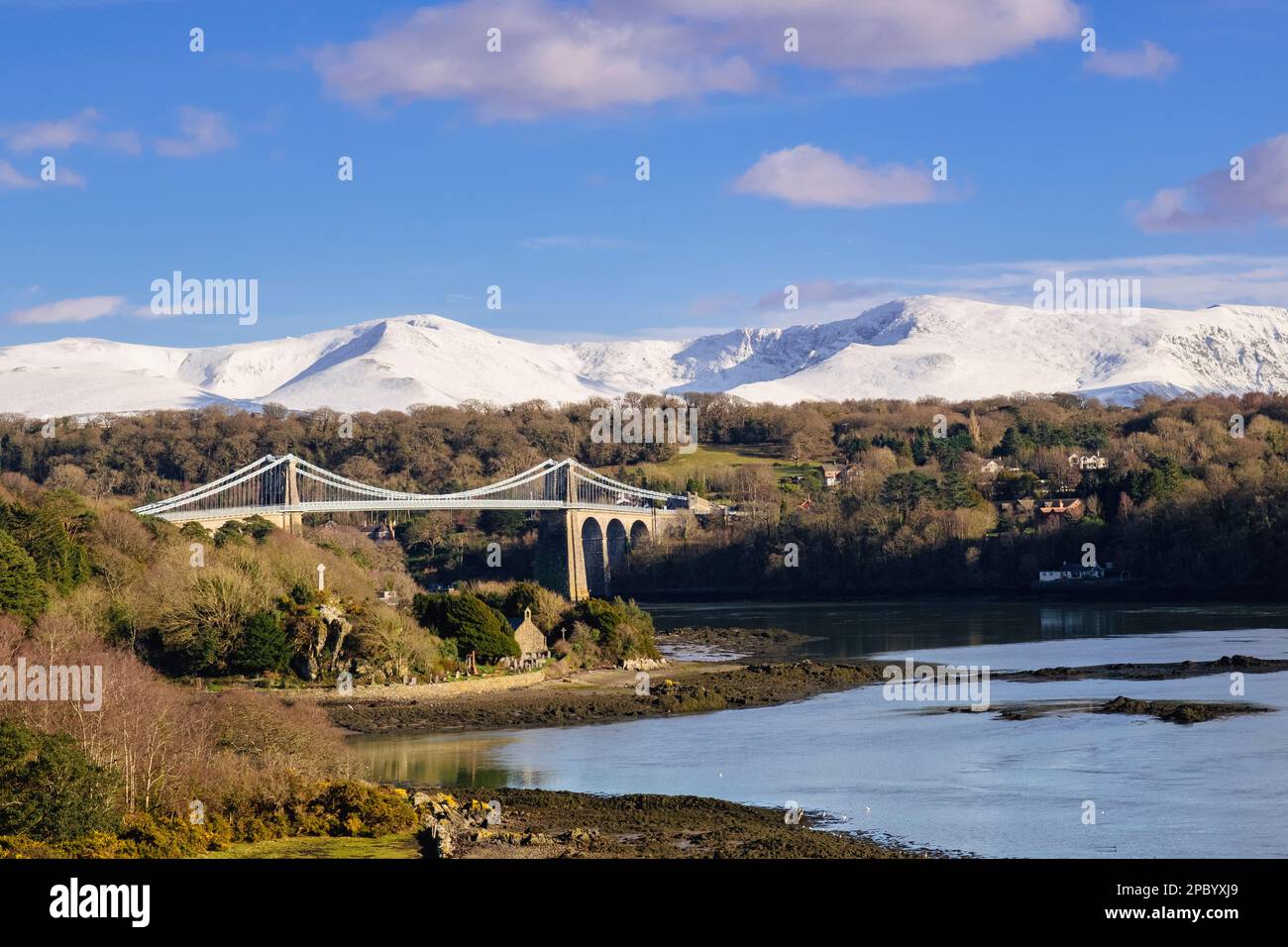 Scenic view to Menai Suspension bridge crossing Menai Strait with snow on mountains in winter. Menai Bridge (Porthaethwy), Isle of Anglesey, Wales, UK Stock Photo