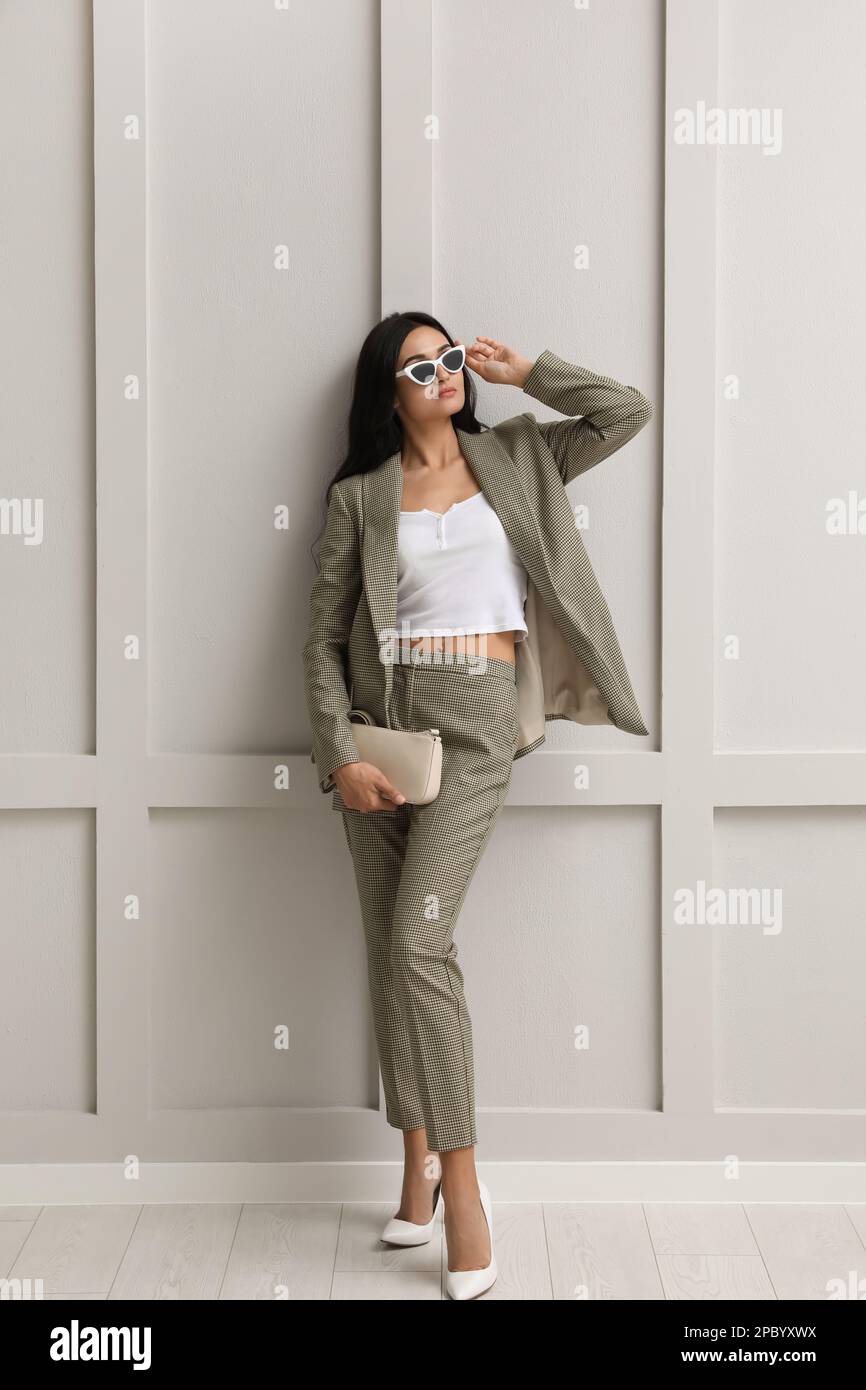 Full length portrait of beautiful woman in formal suit near light grey