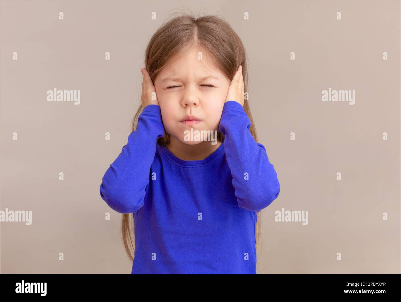 Child with closing ears by hands with closed eyes, isolated on white background waist up caucasian little girl of 5 years in blue Stock Photo