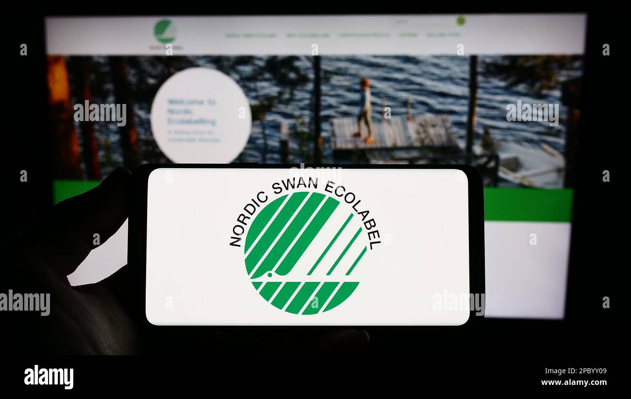 Person holding smartphone with logo of environmental certification Nordic Ecolabel on screen in front of website. Focus on phone display. Stock Photo