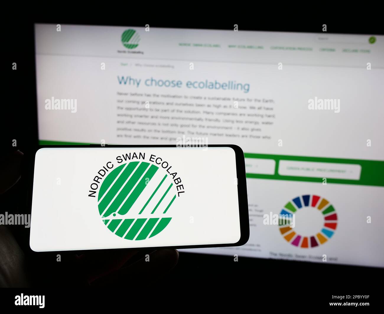 Person holding mobile phone with logo of environmental certification Nordic Ecolabel on screen in front of web page. Focus on phone display. Stock Photo