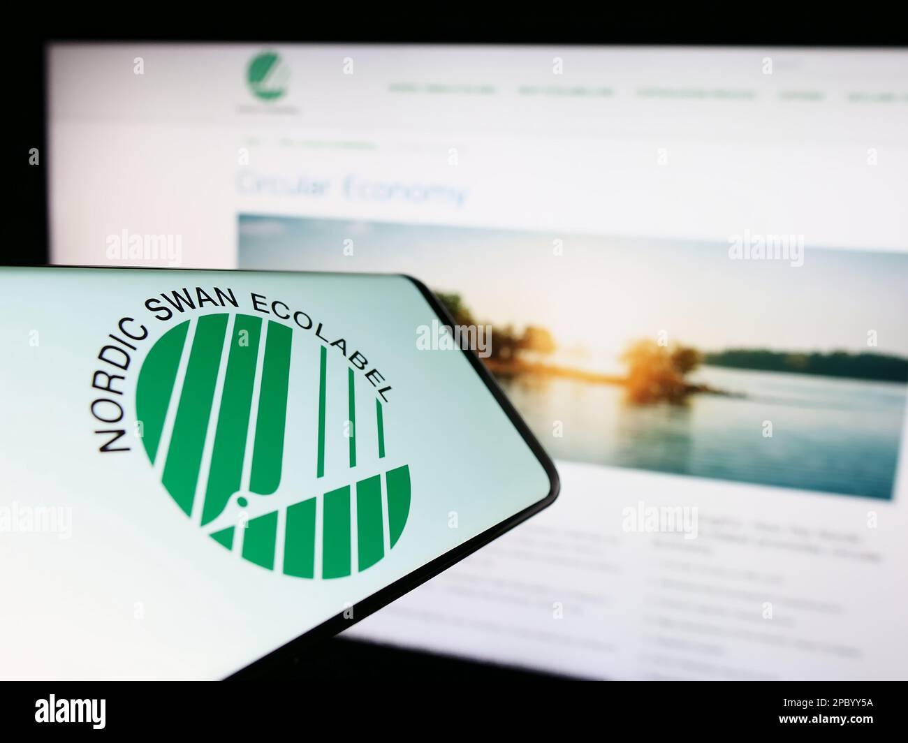 Mobile phone with logo of environmental certification Nordic Ecolabel on screen in front of website. Focus on center-right of phone display. Stock Photo