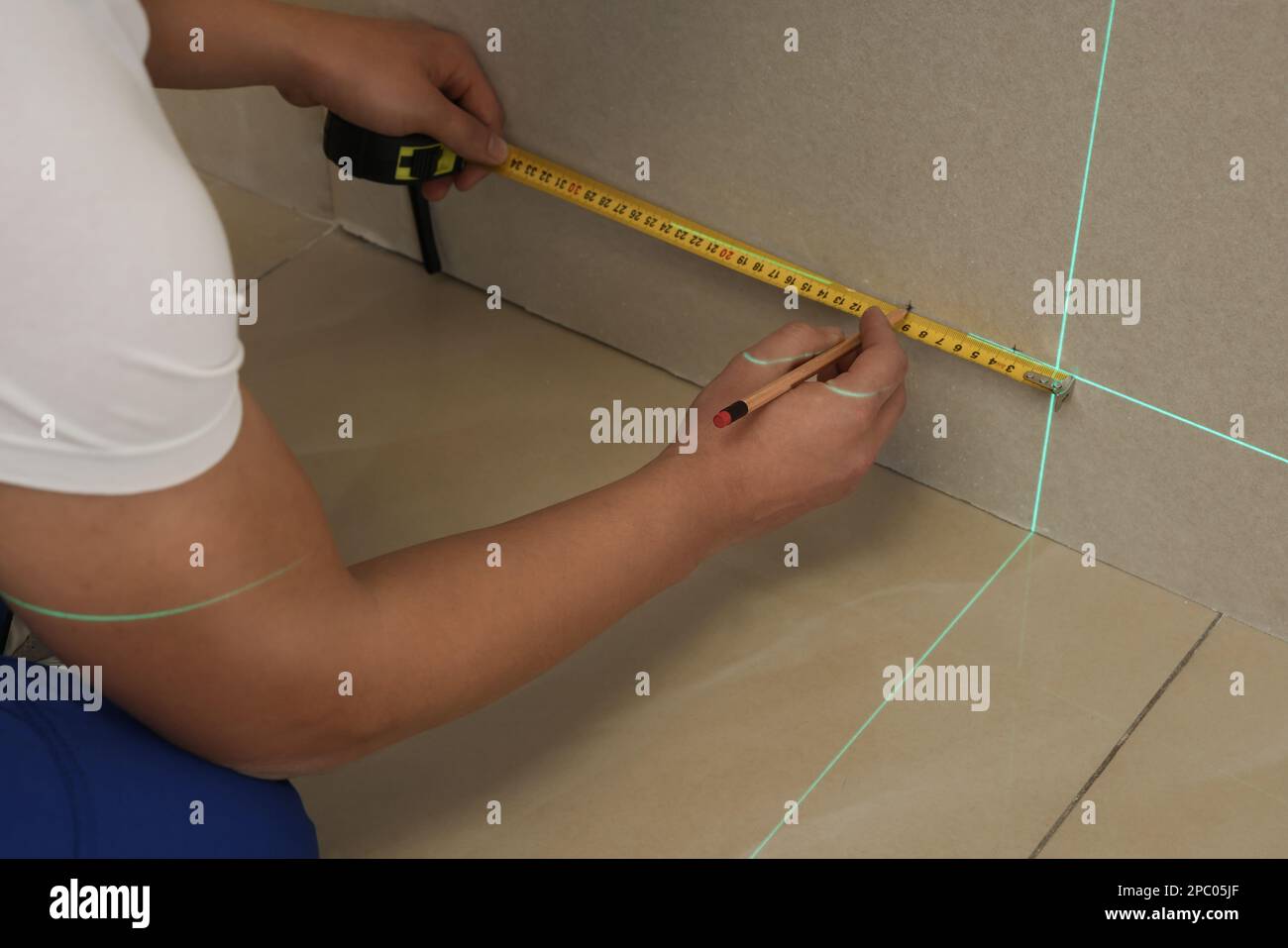 Worker using cross line laser level, pencil and tape for accurate measurement on plasterboard, closeup Stock Photo