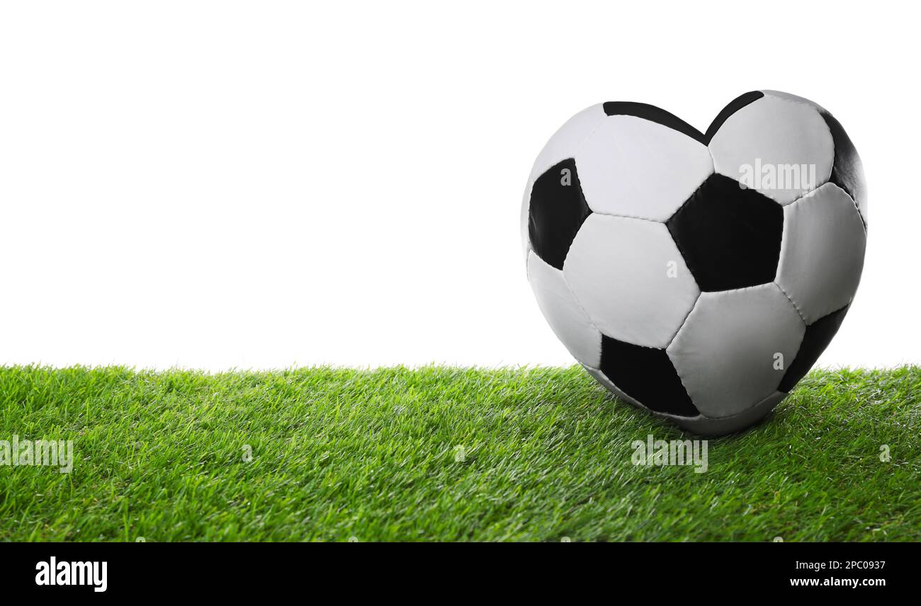 Heart shaped soccer ball on green grass against white background. Space