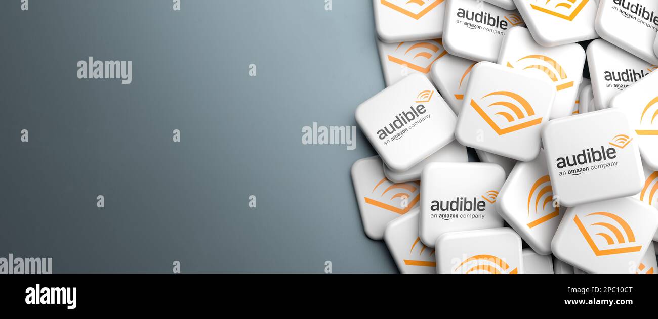 Logos of Audible the audio book and podcast service by Amazon on a heap on a table. Copy space. Web banner format. Stock Photo