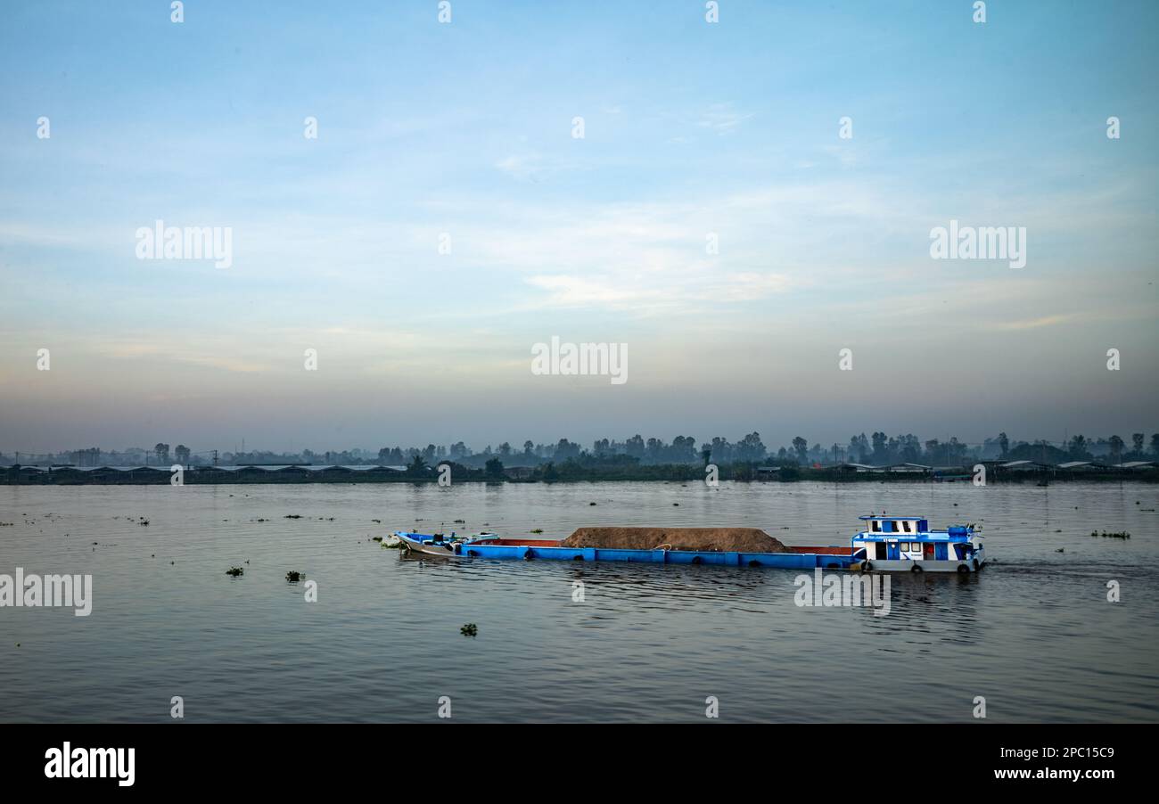 A barge loaded with sand dredged from the Mekong River bed makes its way through the Mekong Delta near Long Xuyen in Vietnam. Stock Photo