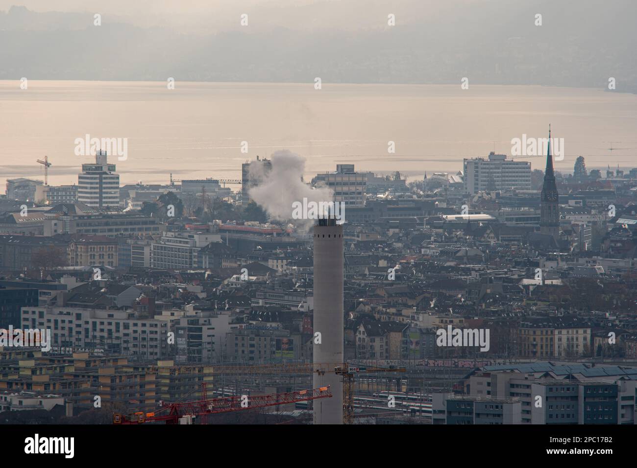 Tall smokestack or industrial chimney emitting white smoke or steam. Zurich city Switzerland, gray cloudy winter day, close-up telephoto shot. Stock Photo