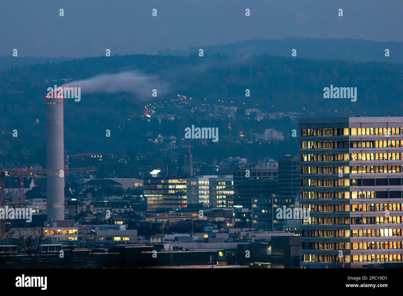Tall smokestack or industrial chimney emitting white smoke or steam. Zurich city Switzerland. Late evening winter day, close-up telephoto shot.. Stock Photo