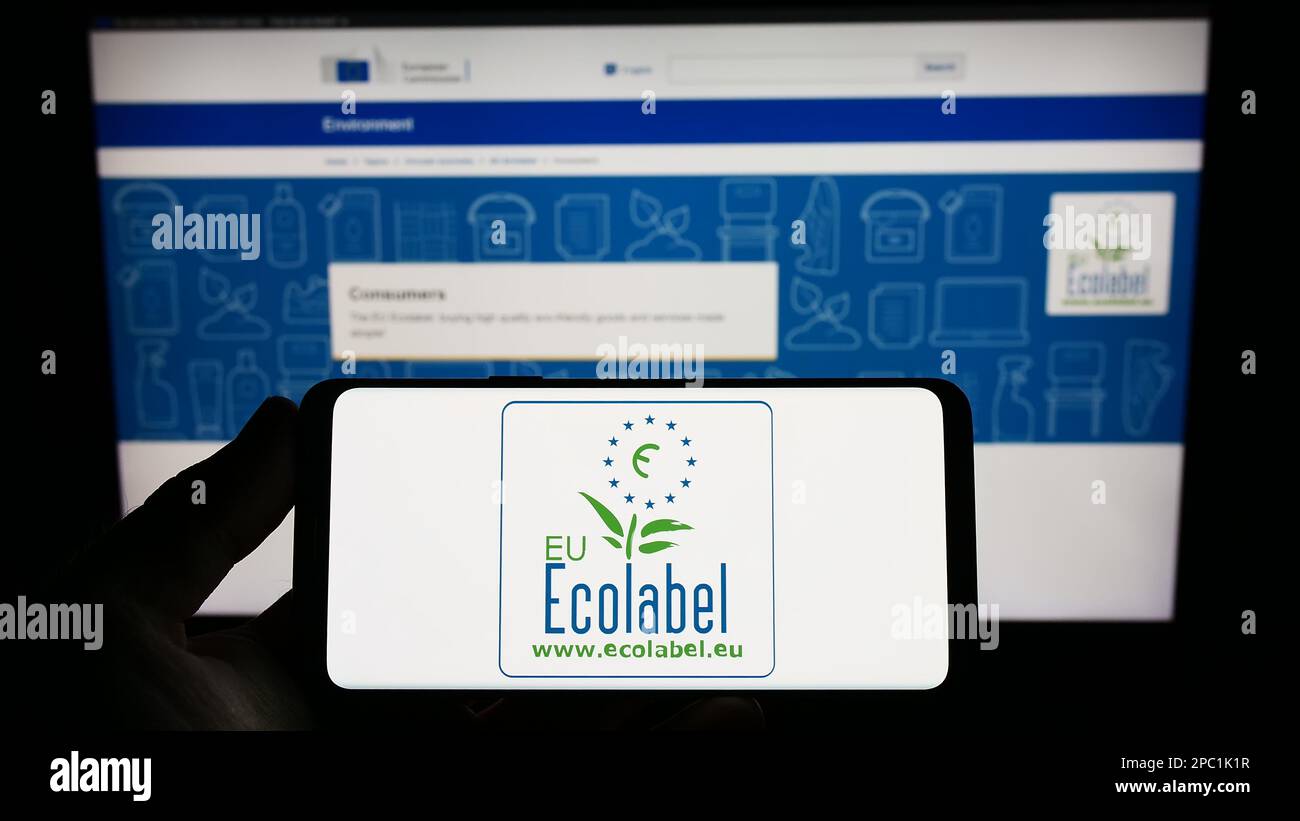 Person holding smartphone with logo of environmental certification EU Ecolabel on screen in front of website. Focus on phone display. Stock Photo