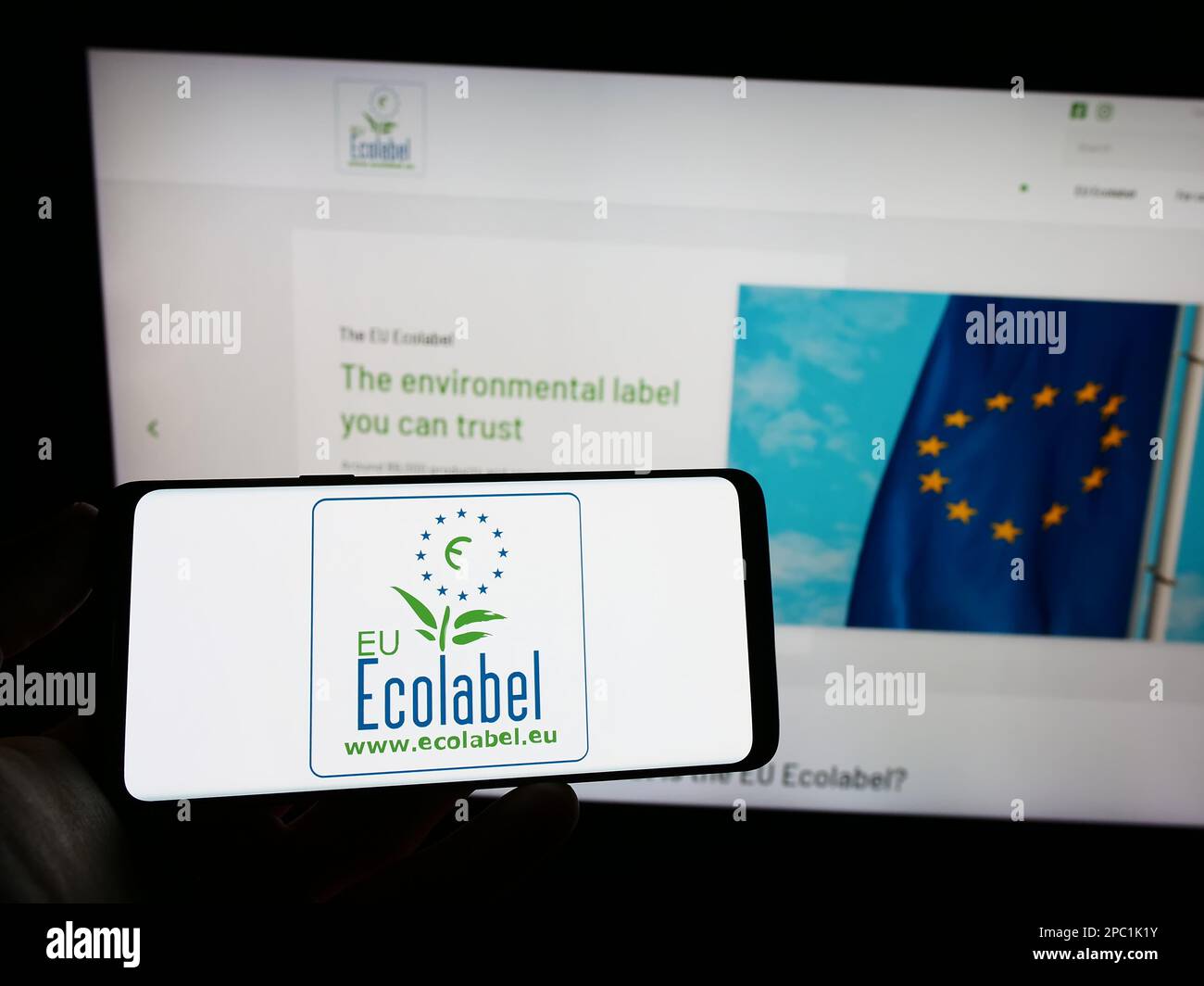 Person holding cellphone with logo of environmental certification EU Ecolabel on screen in front of webpage. Focus on phone display. Stock Photo