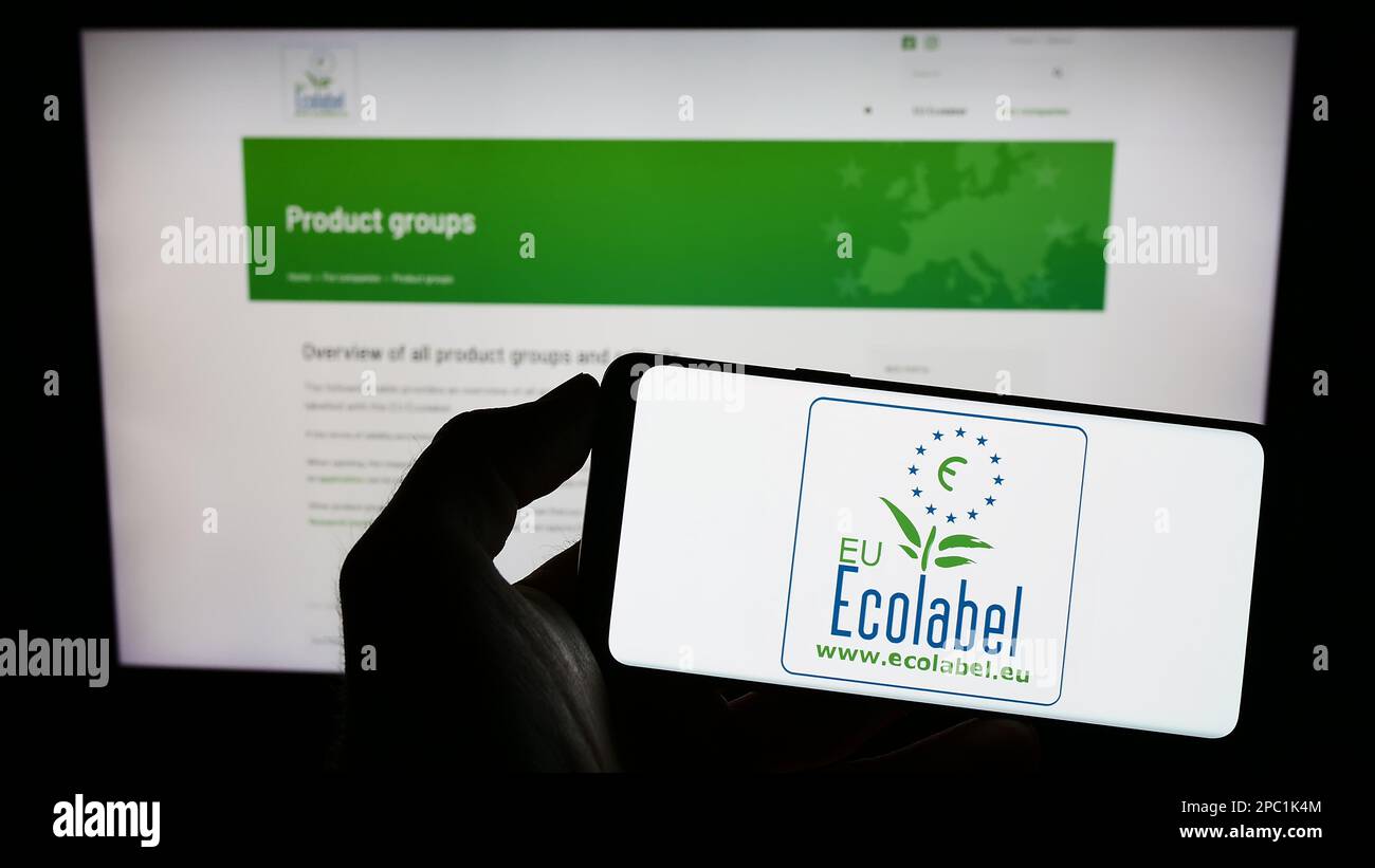 Person holding mobile phone with logo of environmental certification EU Ecolabel on screen in front of web page. Focus on phone display. Stock Photo