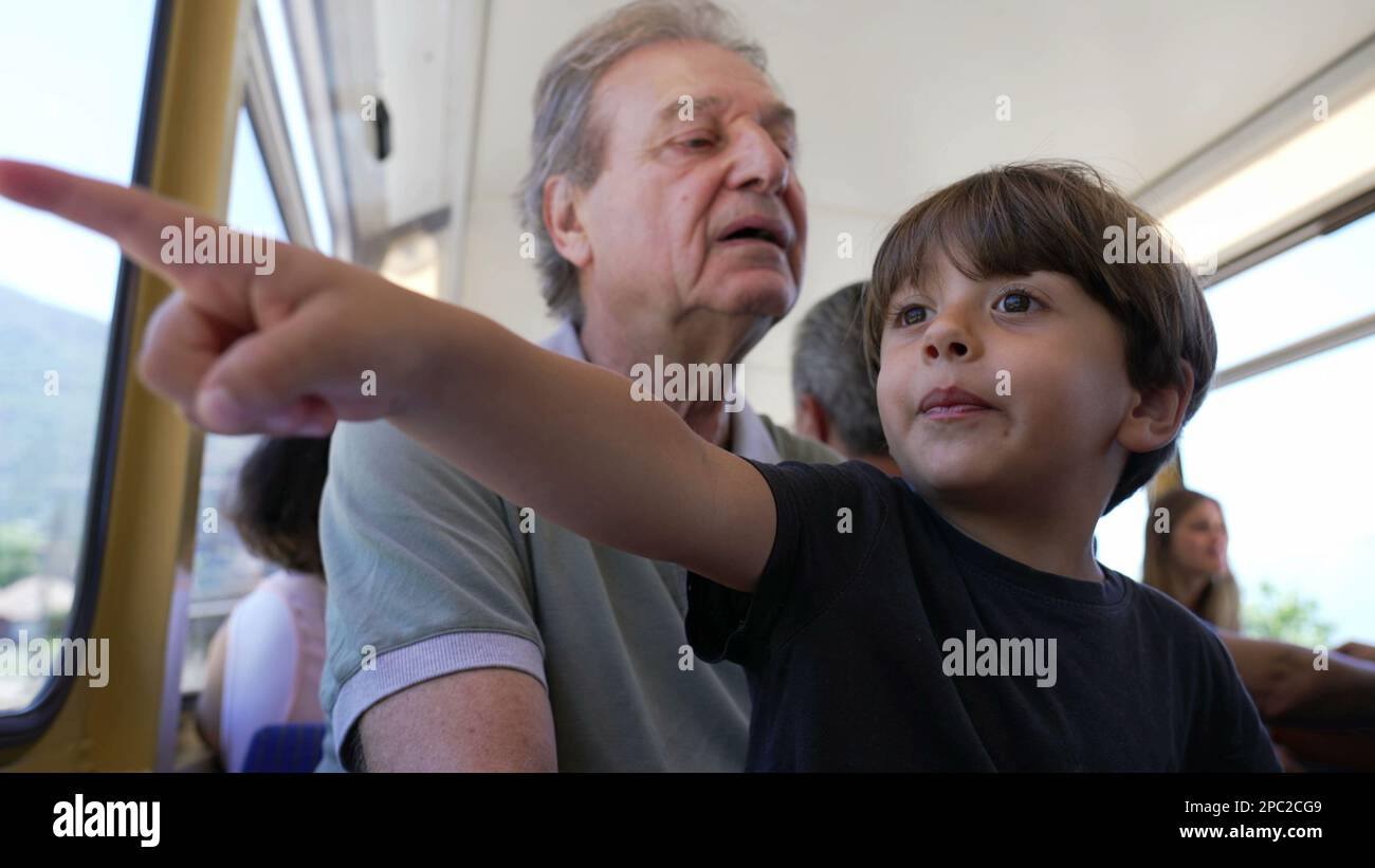 Grandfather traveling by train with grandchild seated by window looking ...