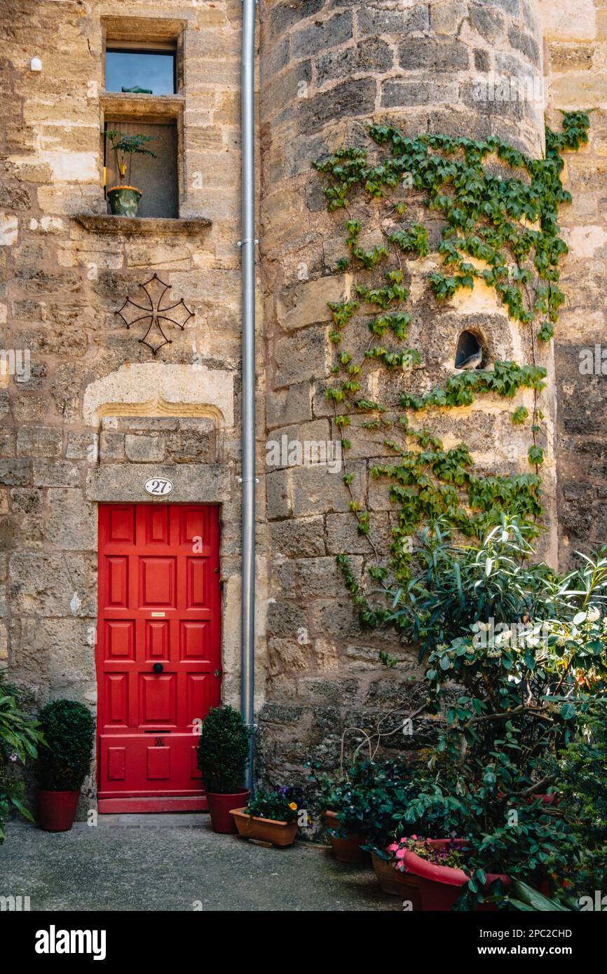 Red door and ivy climbing on the stone tower of a medieval house in Pezenas old town in the south of France (Herault) Stock Photo