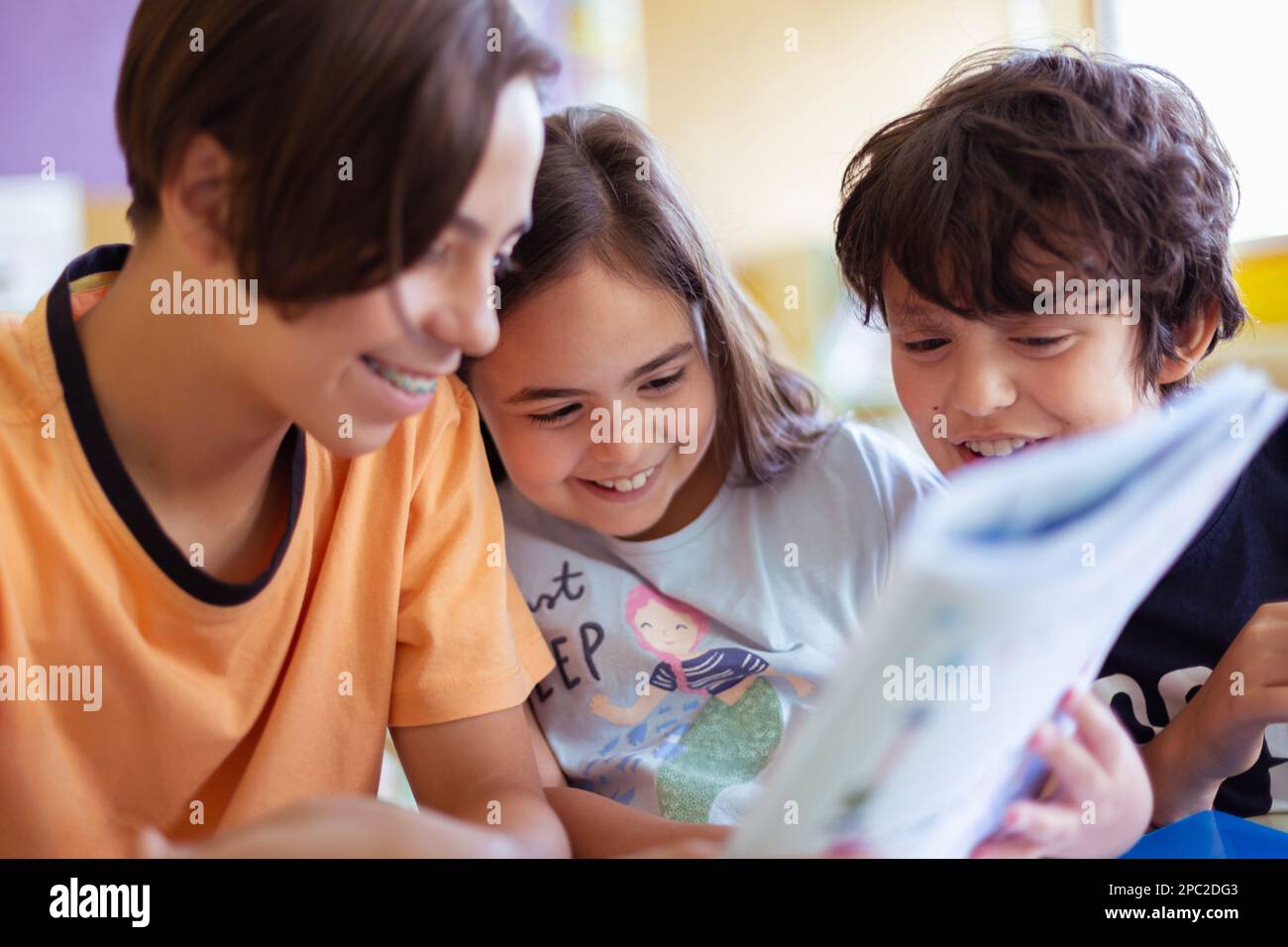 Group of Caucasian children studying fun in class. They are smiling while reading a school book. Stock Photo