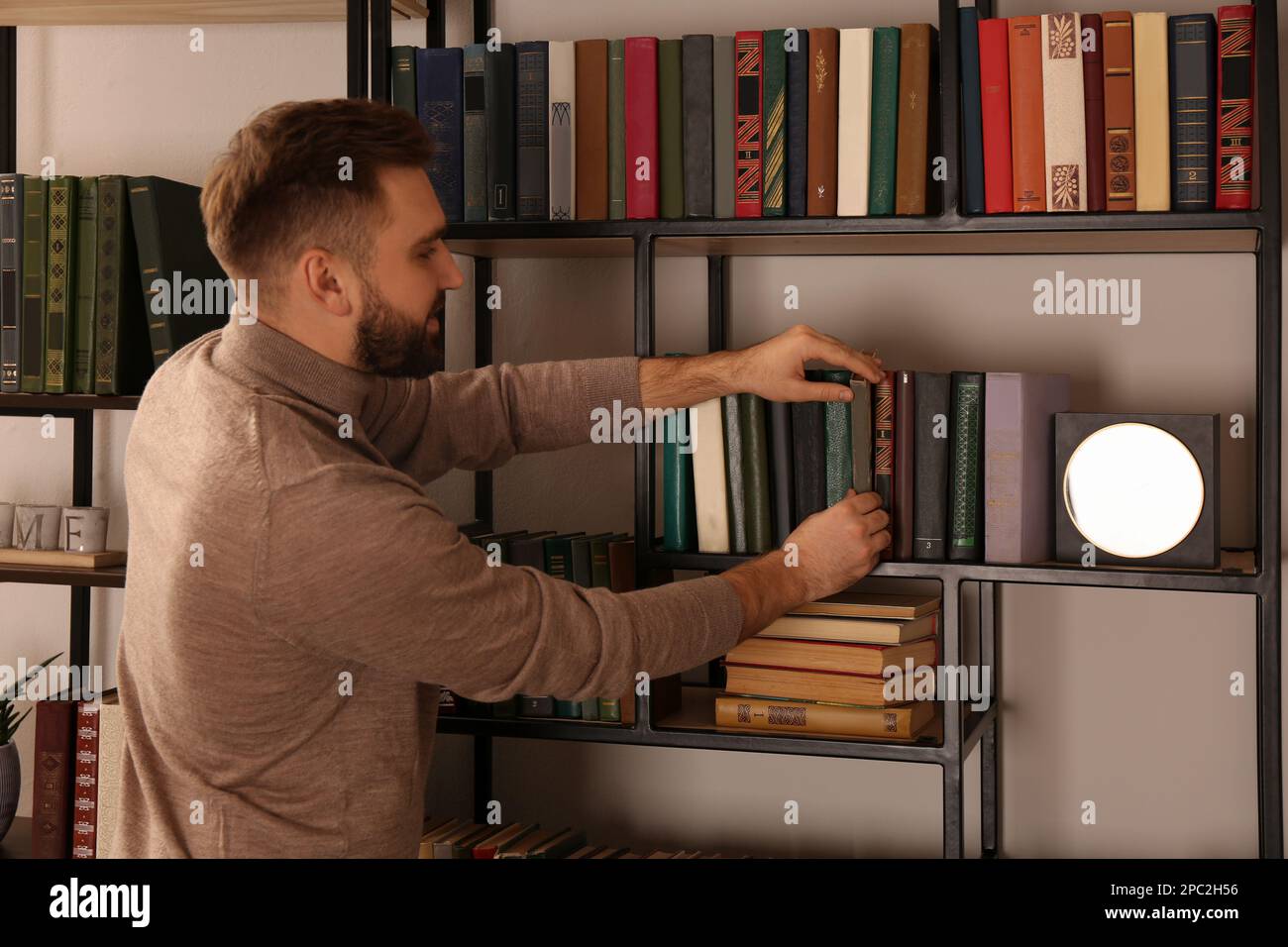 Young man choosing book on shelf in home library Stock Photo