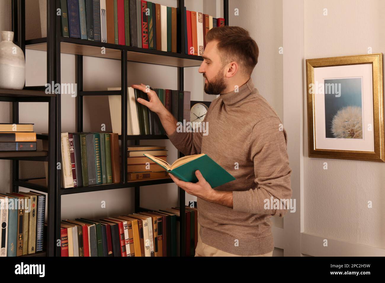 Young man choosing book on shelf in home library Stock Photo