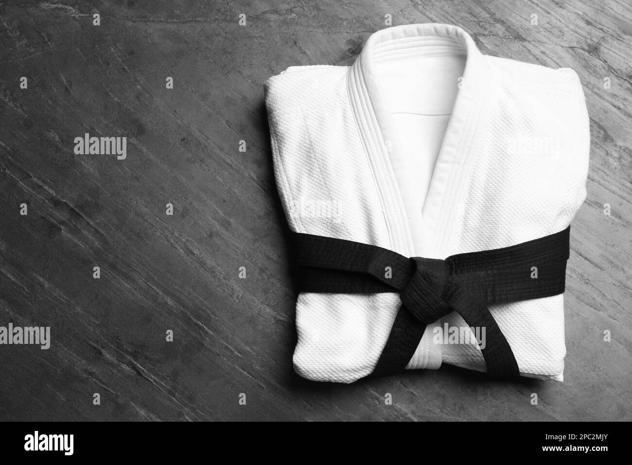 Martial arts uniform with black belt on grey stone background, top view